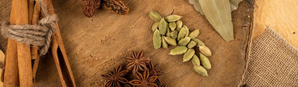 A collection of Indian spices including cardamom, star anise, and bay leaves on a wooden board.